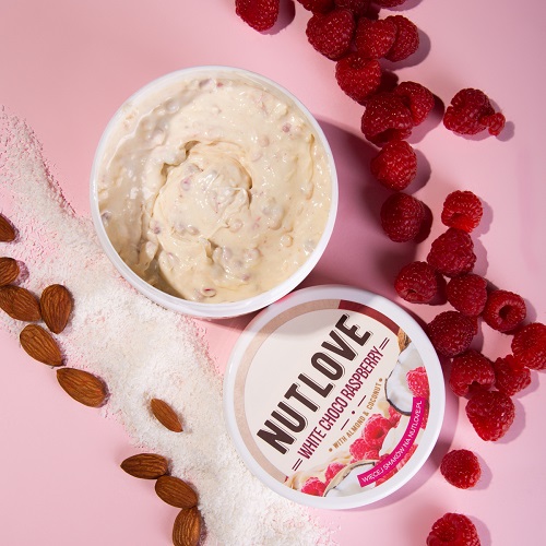 Allnutrition Nutlove White Choco Raspberry 500g nut cream with visible raspberries, almonds, and coconut flakes, in a white round tub on a pink background.