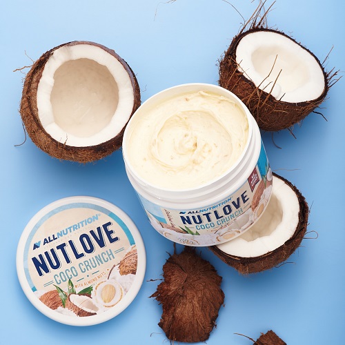 Allnutrition Nutlove Coco Crunch 500g coconut and almond nut spread, creamy texture, white color, surrounded by fresh coconuts, on a light blue background.